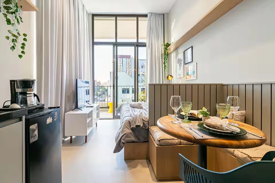 Studio com cozinha compacta, cama, mesa para duas pessoas e varanda com vista da cidade