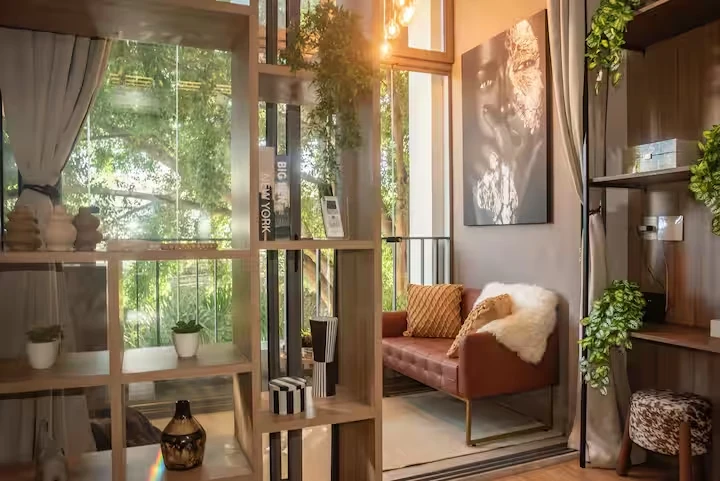 Sala com sofá de couro, estante com plantas e janela voltada para as árvores